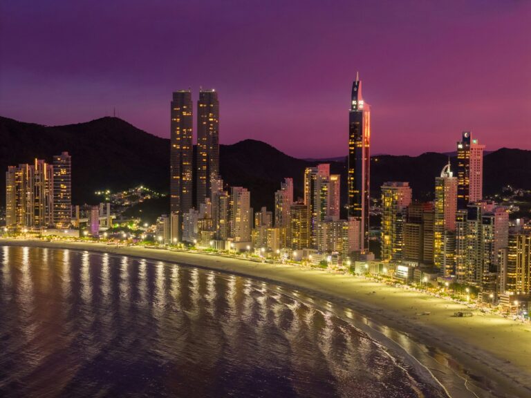 a city skyline at night with a beach and mountains in the background